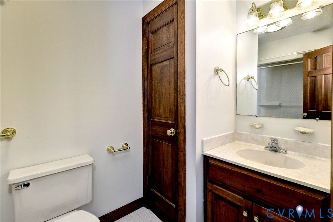14151 Black Horse Lane, Lanexa, VA 23089 Vanity featuring a stone-composite countertop with an integrated oval basin, natural wood-finish cabinetry, solid wood door, and polished brass fixtures