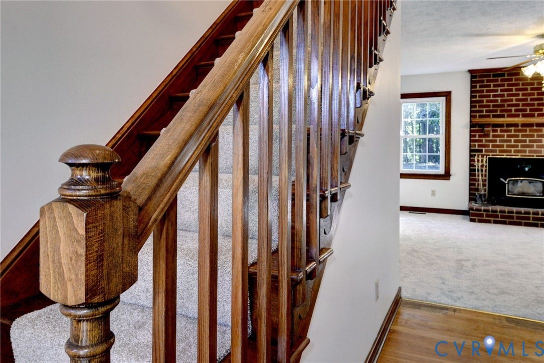 14151 Black Horse Lane, Lanexa, VA 23089 Staircase featuring stained wood balusters and a decorative newel post, with a red brick fireplace and wood-finish flooring