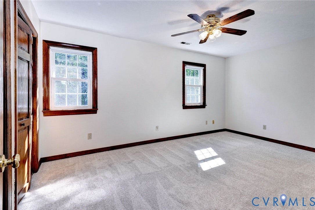 14151 Black Horse Lane, Lanexa, VA 23089 Neutral interior space featuring carpeted flooring, two multi-pane windows with wood-finish trim, a wood-finish interior door, and a ceiling-mounted light fixture with fan blades