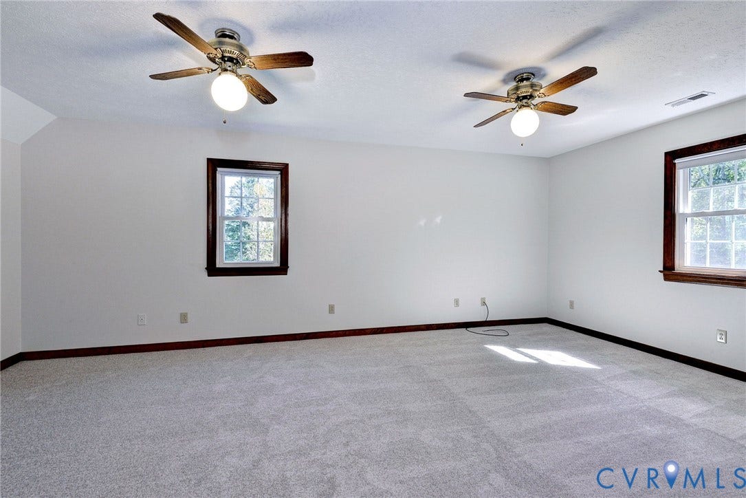 14151 Black Horse Lane, Lanexa, VA 23089 Spacious interior featuring wall-to-wall carpeting, two ceiling fans with integrated light fixtures, and dual windows finished with wood-toned trim