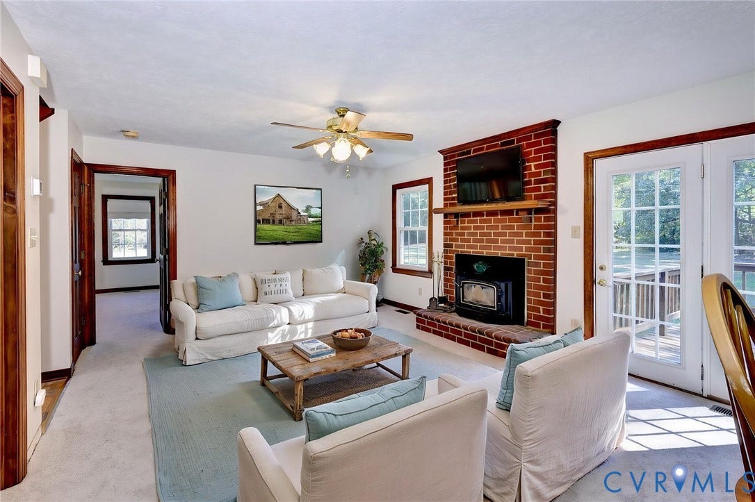 14151 Black Horse Lane, Lanexa, VA 23089 - VIRTUAL STAGING Living area featuring a floor-to-ceiling red brick fireplace, wood-cased window trim, ceiling fan with integrated lighting, and glass-paneled double doors