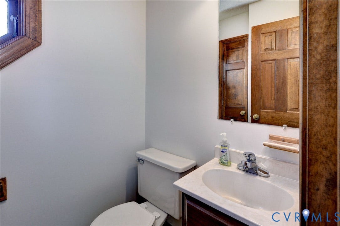 14151 Black Horse Lane, Lanexa, VA 23089 Vanity featuring a stone-composite countertop, oval undermount sink, chrome faucet, and wood-finish cabinetry, paired with a wood-framed mirror