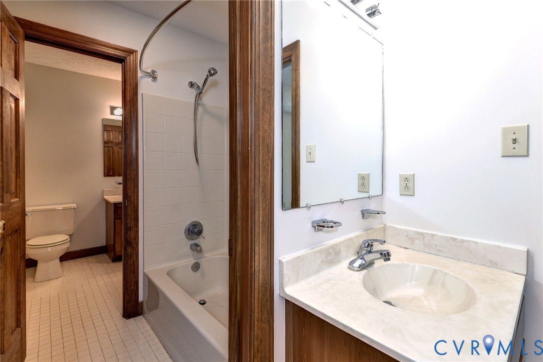 14151 Black Horse Lane, Lanexa, VA 23089 Bathroom vanity featuring a solid-surface countertop with an integrated basin, wall-mounted mirror, ceramic tile flooring, and a bathtub with a tiled surround