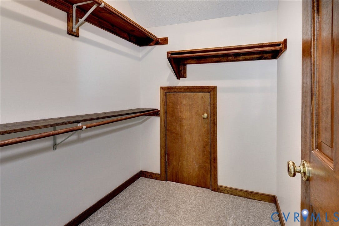 14151 Black Horse Lane, Lanexa, VA 23089 Walk-in storage space featuring built-in wood shelving, integrated garment rods, neutral carpeting, and a dedicated access door with a metallic knob