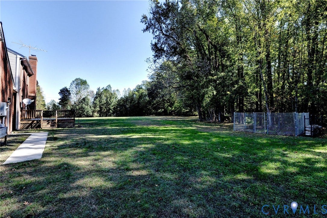 14151 Black Horse Lane, Lanexa, VA 23089 Expansive backyard featuring a concrete walkway, elevated wood deck, and perimeter chain-link fencing, bordered by mature trees