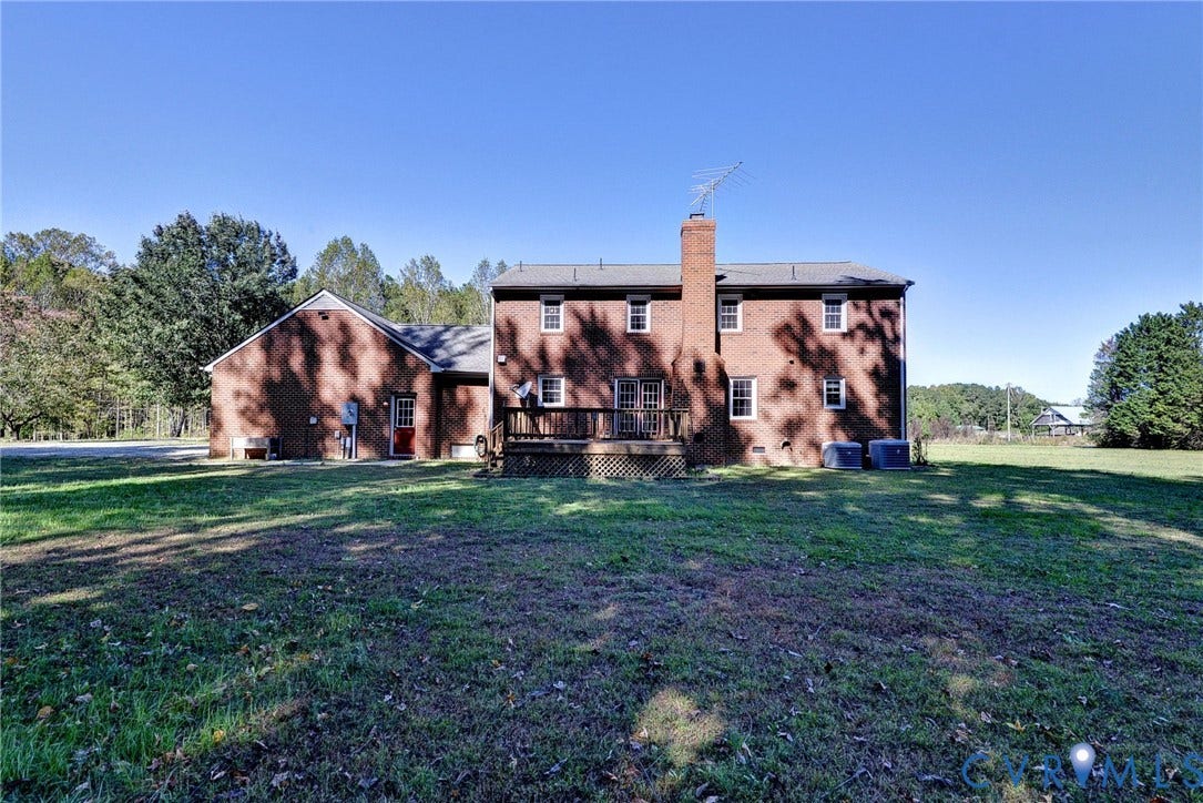 14151 Black Horse Lane, Lanexa, VA 23089 Two-story brick exterior featuring a rear wood deck, prominent masonry chimney, and expansive surrounding grounds