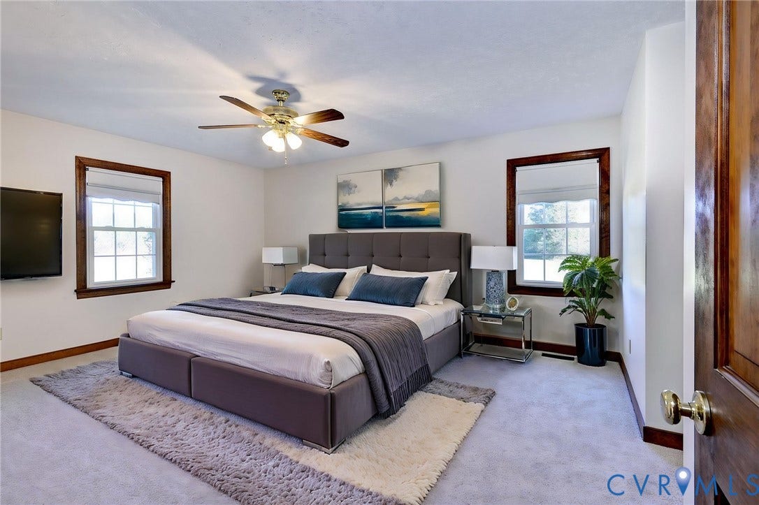 14151 Black Horse Lane, Lanexa, VA 23089 VIRTUAL STAGING - Spacious room featuring neutral carpeting, two windows with stained-wood trim, and a multi-blade ceiling fan with integrated lighting