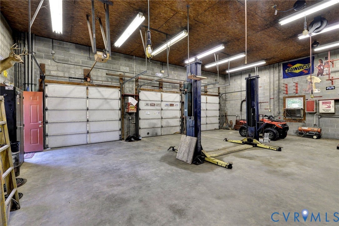 14151 Black Horse Lane, Lanexa, VA 23089 Spacious garage featuring three overhead doors, concrete flooring, exposed masonry walls, and a professional-grade automotive lift
