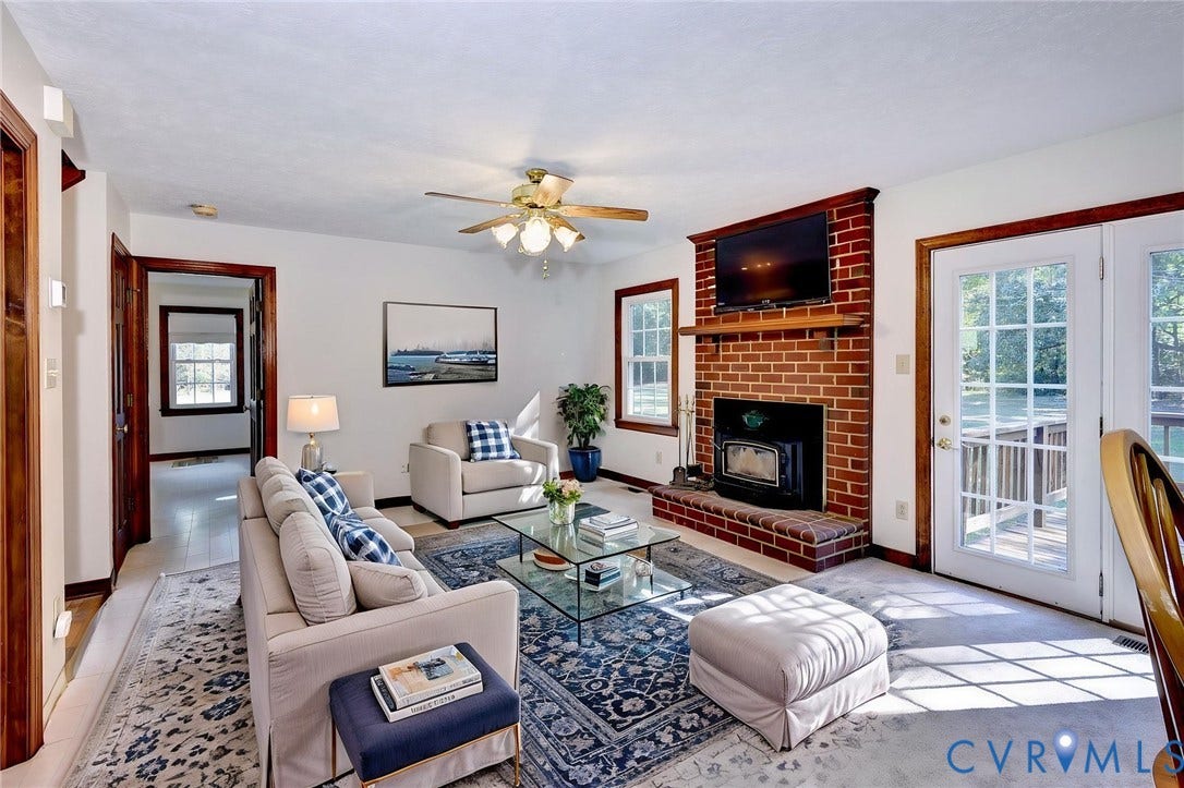 14151 Black Horse Lane, Lanexa, VA 23089 VIRTUAL STAGING - Living area featuring a floor-to-ceiling red brick fireplace, a hearth with an inset wood stove, dual glass-paned doors, and a ceiling fan with integrated lighting