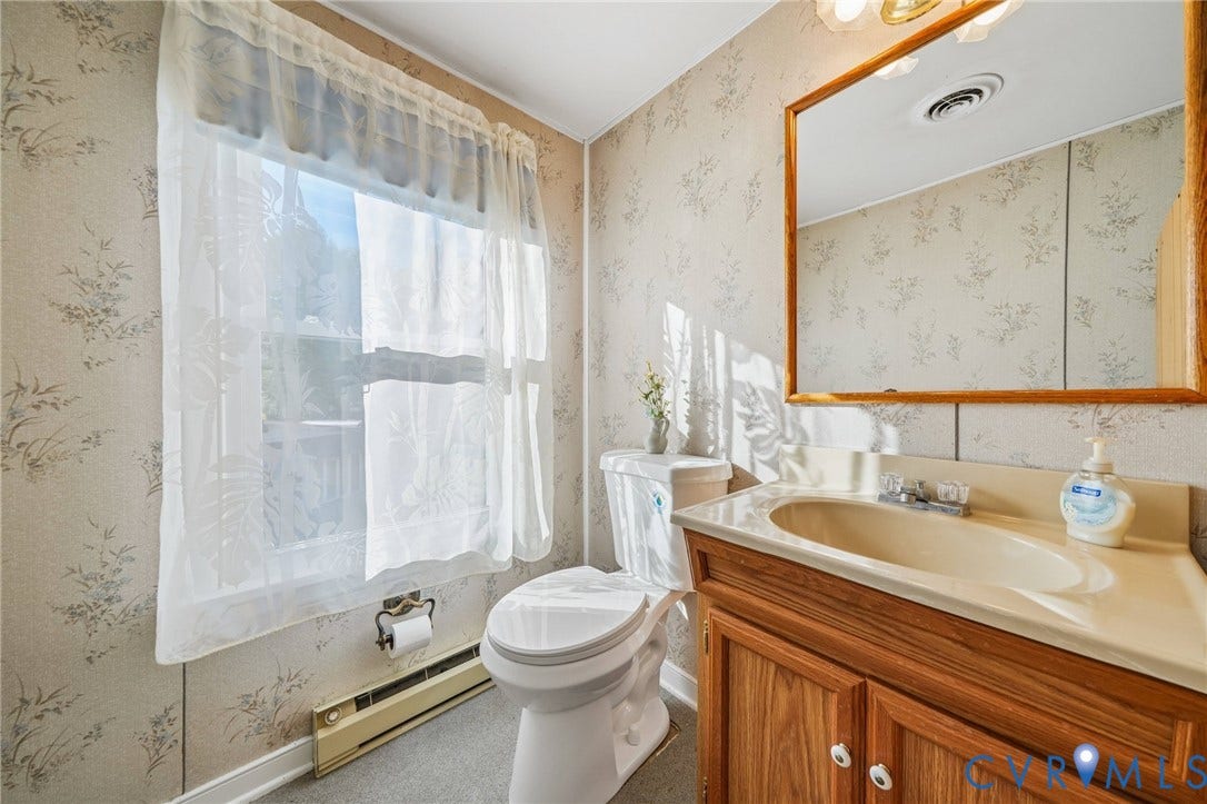 3030 Brentwood Circle, Chesterfield, VA 23237 Bathroom featuring a wood-toned vanity with an integrated basin, a large framed wall mirror, patterned wallpaper, and a window with natural light