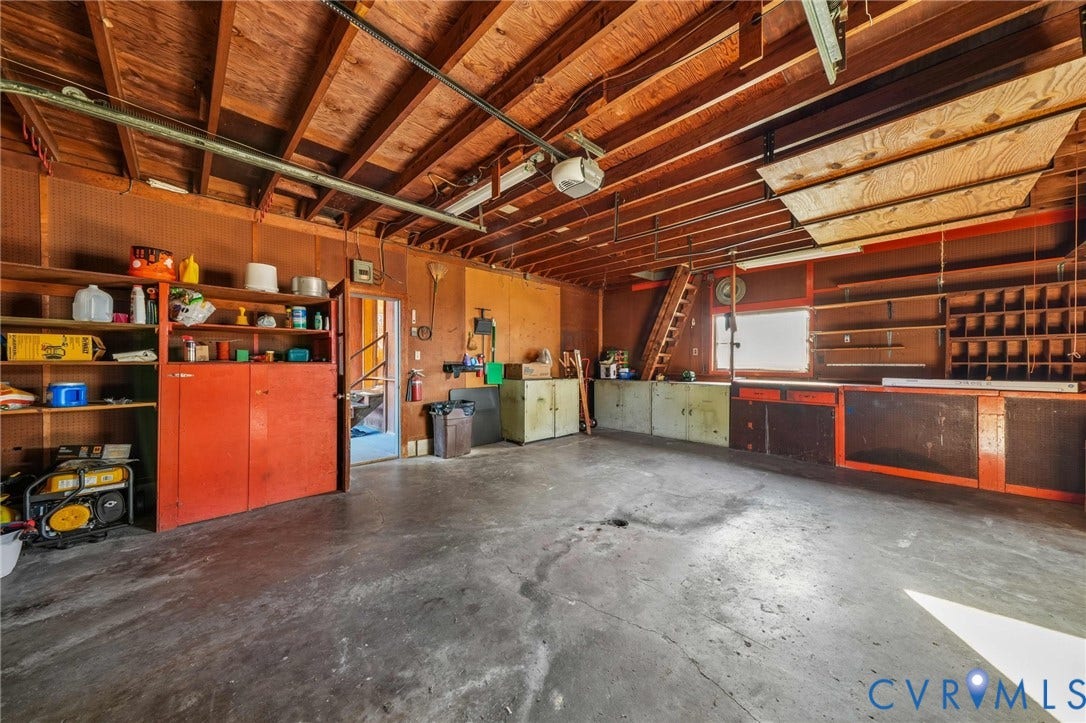 3030 Brentwood Circle, Chesterfield, VA 23237 Multi-car garage featuring exposed wood ceiling joists, concrete flooring, extensive built-in storage cabinetry, open wall-mounted shelving