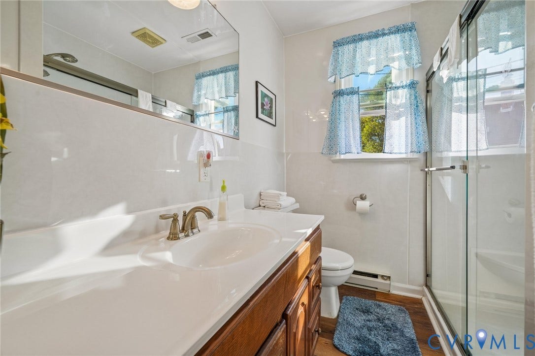 3030 Brentwood Circle, Chesterfield, VA 23237 First floor Bathroom featuring a wood-finish vanity with an integrated basin, a large wall-mounted mirror, a glass-enclosed shower, and wood-finish flooring