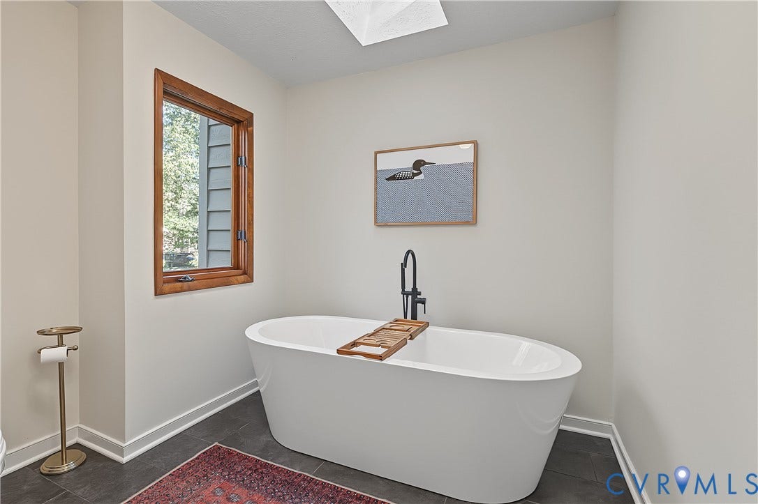 3800 Pheasant Hollow Drive, Henrico, VA 23231 Freestanding white soaking tub with matte black floor-mounted faucet and skylight overhead, featuring dark tile flooring and wood-trimmed window