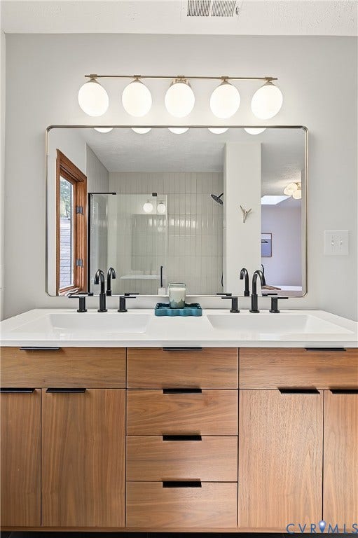 3800 Pheasant Hollow Drive, Henrico, VA 23231 Dual-sink vanity featuring wood-finish cabinetry, rectangular integrated basins, matte black widespread faucets, and a broad rectangular mirror illuminated by a five-globe fixture