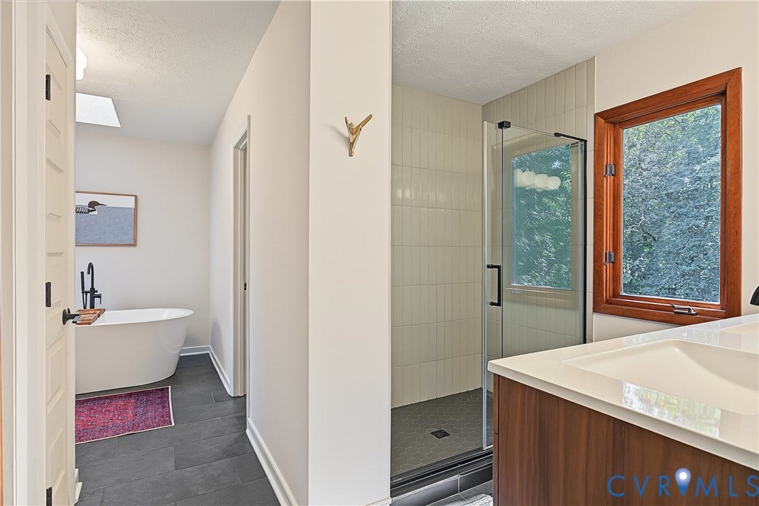 3800 Pheasant Hollow Drive, Henrico, VA 23231 Freestanding soaking tub with matte black faucet, walk-in shower with vertical tile surround, wood-finish vanity with integrated sink, dark large-format floor tile, and wood-framed window