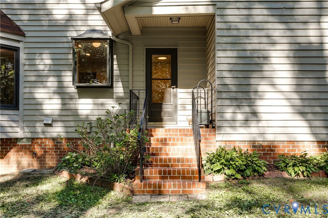 3800 Pheasant Hollow Drive, Henrico, VA 23231 Exterior entrance featuring horizontal lap siding, brick foundation, recessed entryway, wrought iron handrails, and a multi-pane bay window