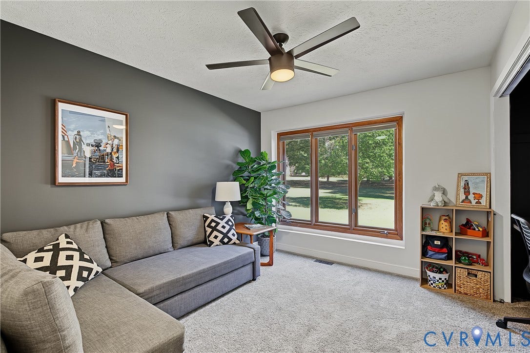 3800 Pheasant Hollow Drive, Henrico, VA 23231 Room featuring a dark-toned accent wall, large picture window with wood trim, ceiling fan with integrated lighting, and neutral carpeting