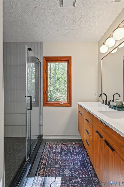 3800 Pheasant Hollow Drive, Henrico, VA 23231 Wood-finish cabinetry with a white countertop and dual undermount sinks, glass-enclosed shower with vertical wall tiling and hexagonal floor tile, and a multi-globe vanity light fixture