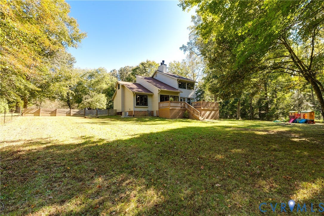 3800 Pheasant Hollow Drive, Henrico, VA 23231 Expansive backyard featuring a leveled grass lawn, mature trees, wood-slat perimeter fencing, and an elevated wood deck