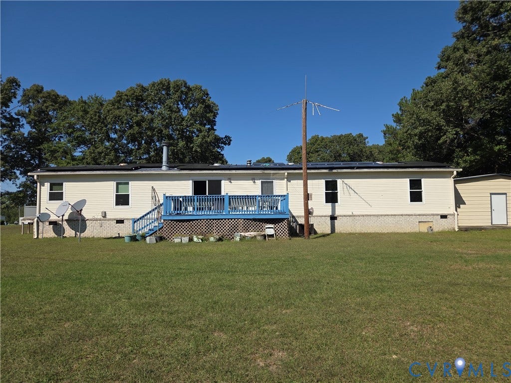 195 Concord Lane, Emporia, VA 23847 Single-level residence with light-colored siding, a raised deck with lattice skirting, and an attached storage structure, set on a grass-covered lot with mature trees