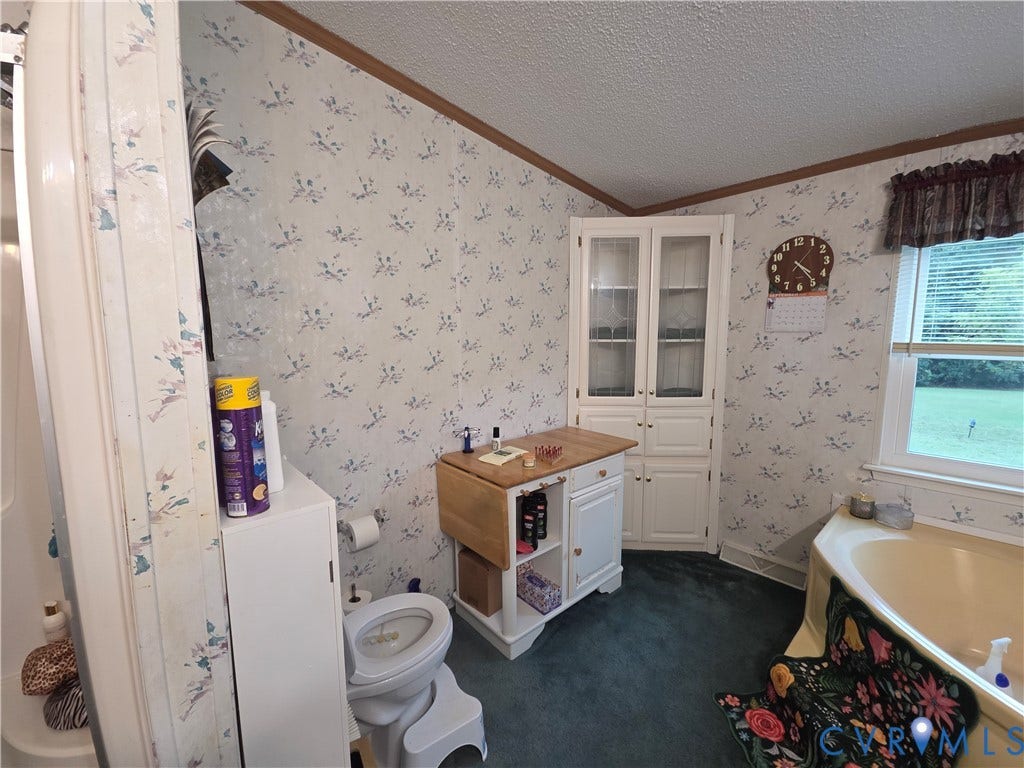 195 Concord Lane, Emporia, VA 23847 Corner built-in cabinetry with glass-front upper doors, soaking tub, window with horizontal blinds, and crown molding