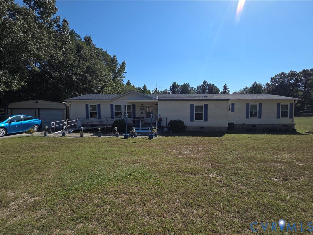 195 Concord Lane, Emporia, VA 23847 Single-level residence featuring light-toned vinyl siding, blue shutters, an asphalt shingle roof, a covered entryway, and a detached two-car metal carport
