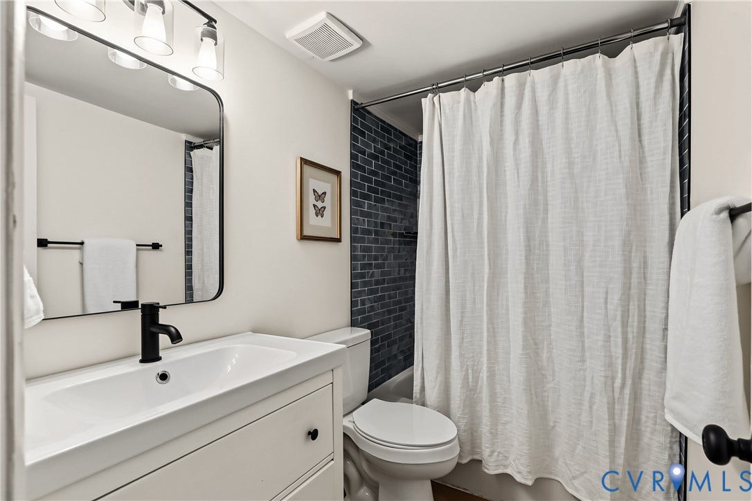 10272 Iron Mill Road, North Chesterfield, VA 23235 Bathroom featuring a white vanity cabinet with a rectangular basin, matte black faucet, rounded rectangular mirror, and dark blue subway tile shower surround