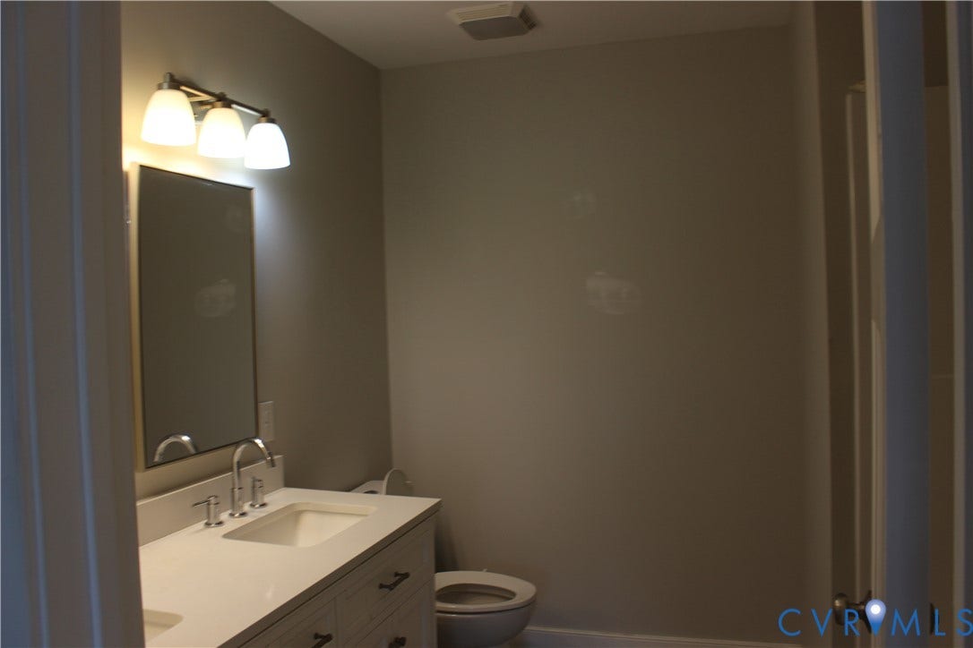 118 Clements Drive, Essex, VA 22560 Bathroom featuring a vanity with a white countertop and integrated sink, a wall-mounted rectangular mirror, a three-light fixture, and a toilet
