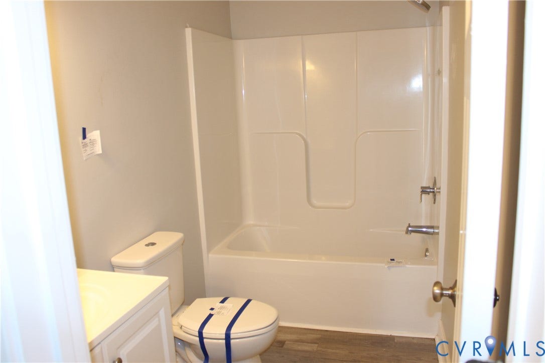 118 Clements Drive, Essex, VA 22560 Bathroom featuring a tub and shower combination with a molded surround, a vanity, a toilet, and wood-finish flooring