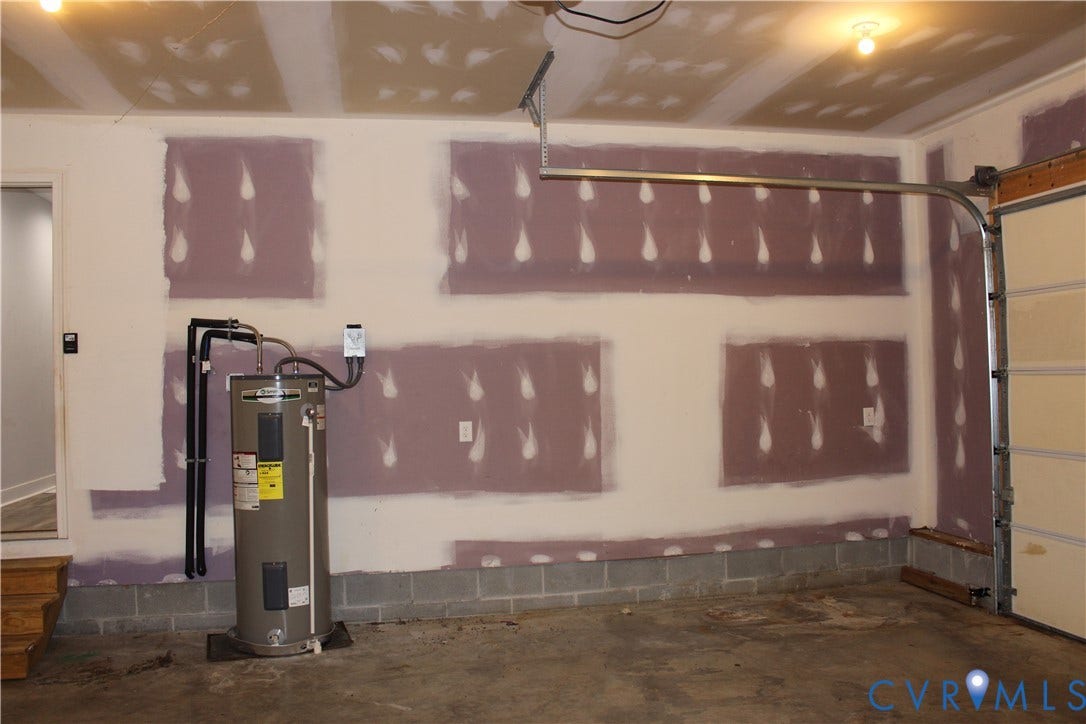 118 Clements Drive, Essex, VA 22560 Garage interior featuring drywall panels, overhead lighting, an upright water heater, and a metal garage door system