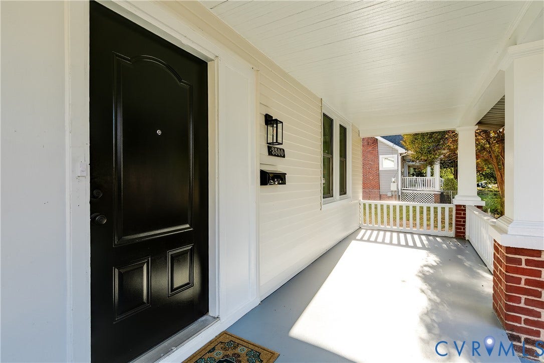 3500 Stockton Street, Weisigers Plan, Richmond, VA 23224 Covered front porch featuring a black panel door, beadboard ceiling, white railing with brick base columns, and wall-mounted exterior lantern lighting