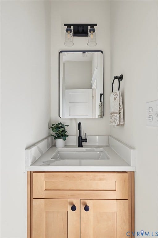 3500 Stockton Street, Weisigers Plan, Richmond, VA 23224 Light-wood finish vanity featuring a solid surface countertop with an integrated basin, matte black faucet, rectangular mirror, and dual-bulb industrial-style wall sconce