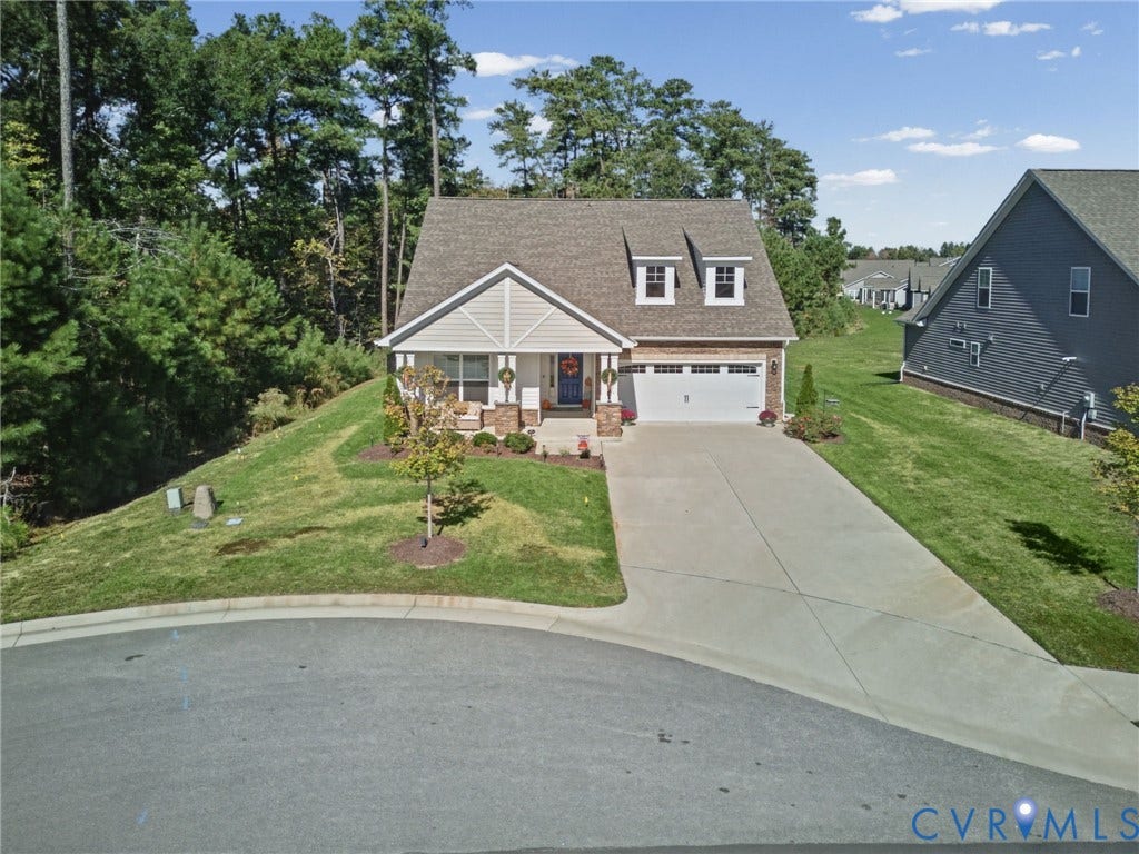 Two-story residence featuring a front-facing attached two-car garage, stone and shingle exterior detailing, gabled roofline with dual dormers, and a concrete driveway