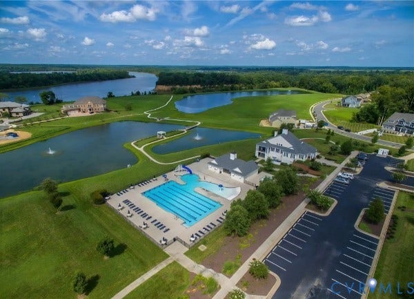 Community amenities featuring a swimming pool, paved parking area, water features, and expansive green space