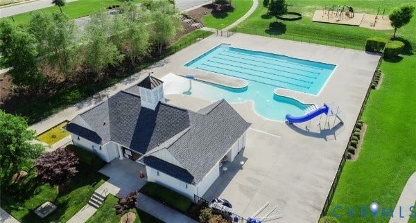 Community recreation center featuring a swimming pool with a slide, concrete pool deck, and a clubhouse with a cupola roof