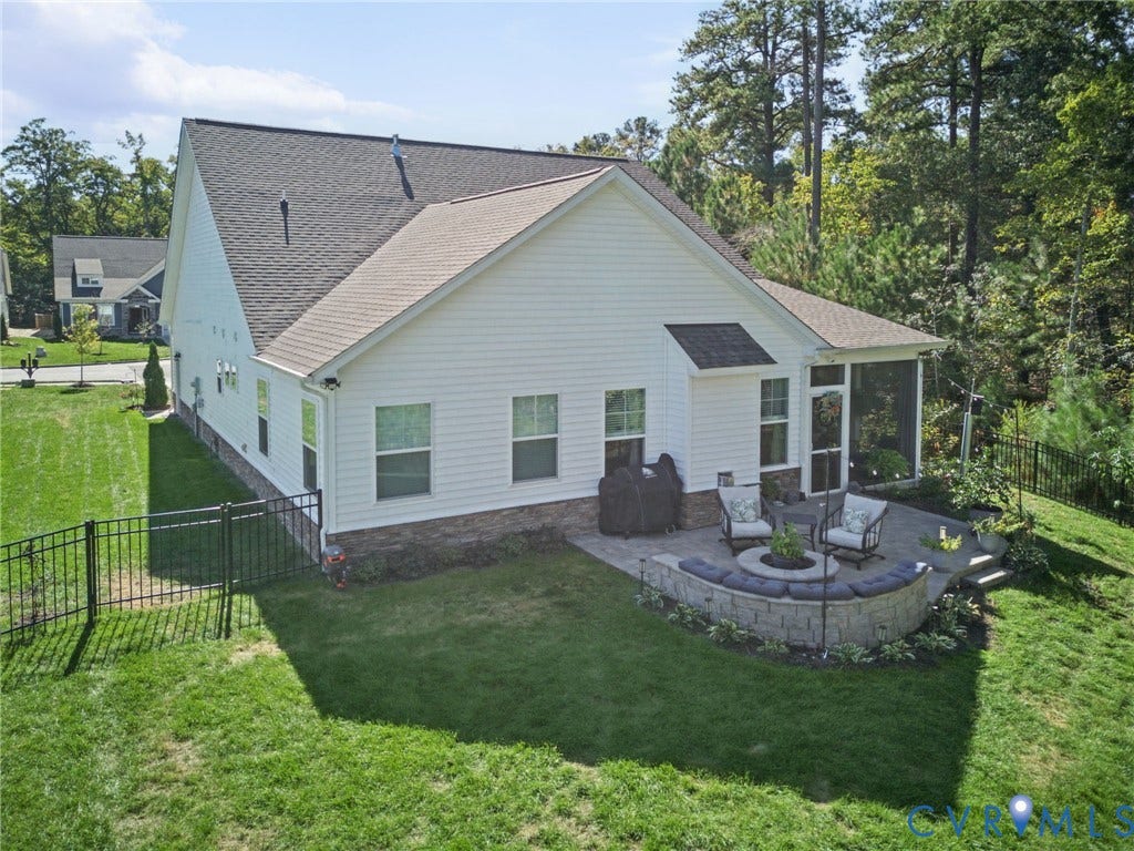 Rear exterior featuring horizontal siding, a stone veneer foundation, a screened porch, a paved patio with a built-in stone fire pit, and a black metal perimeter fence