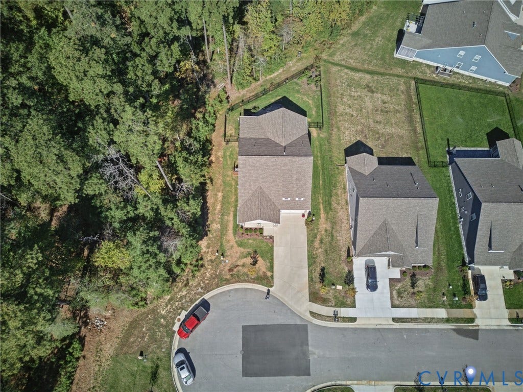 Aerial perspective featuring a lot situated at the end of a cul-de-sac, asphalt driveway, asphalt shingle roofing, and established perimeter tree line