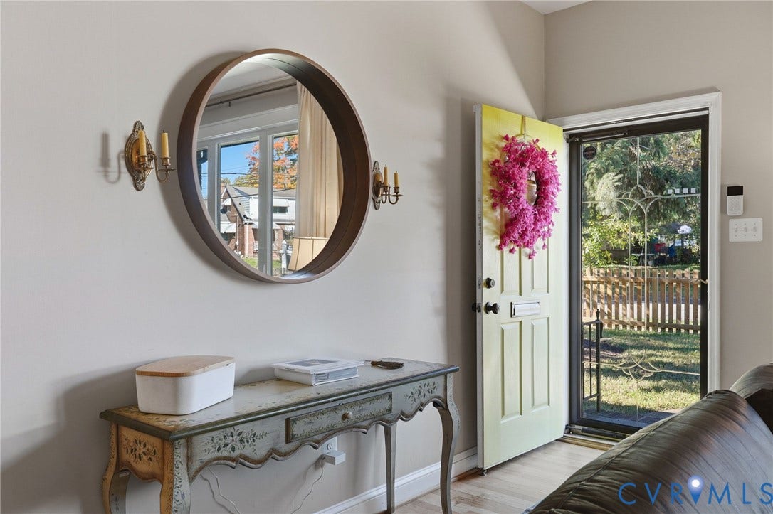 9 E 31st Street, Richmond, VA 23224 Entryway featuring a solid door with a built-in mail slot, a screen door with decorative metal grillwork, two wall-mounted metallic candle-style sconces, and wood-finish flooring