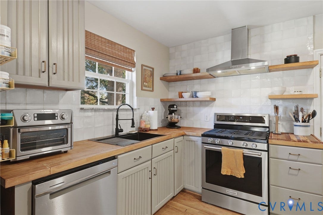9 E 31st Street, Richmond, VA 23224 Kitchen featuring wood countertops, white tiled backsplash, stainless steel gas range with overhead ventilation, beadboard-style cabinetry, and floating wood shelving
