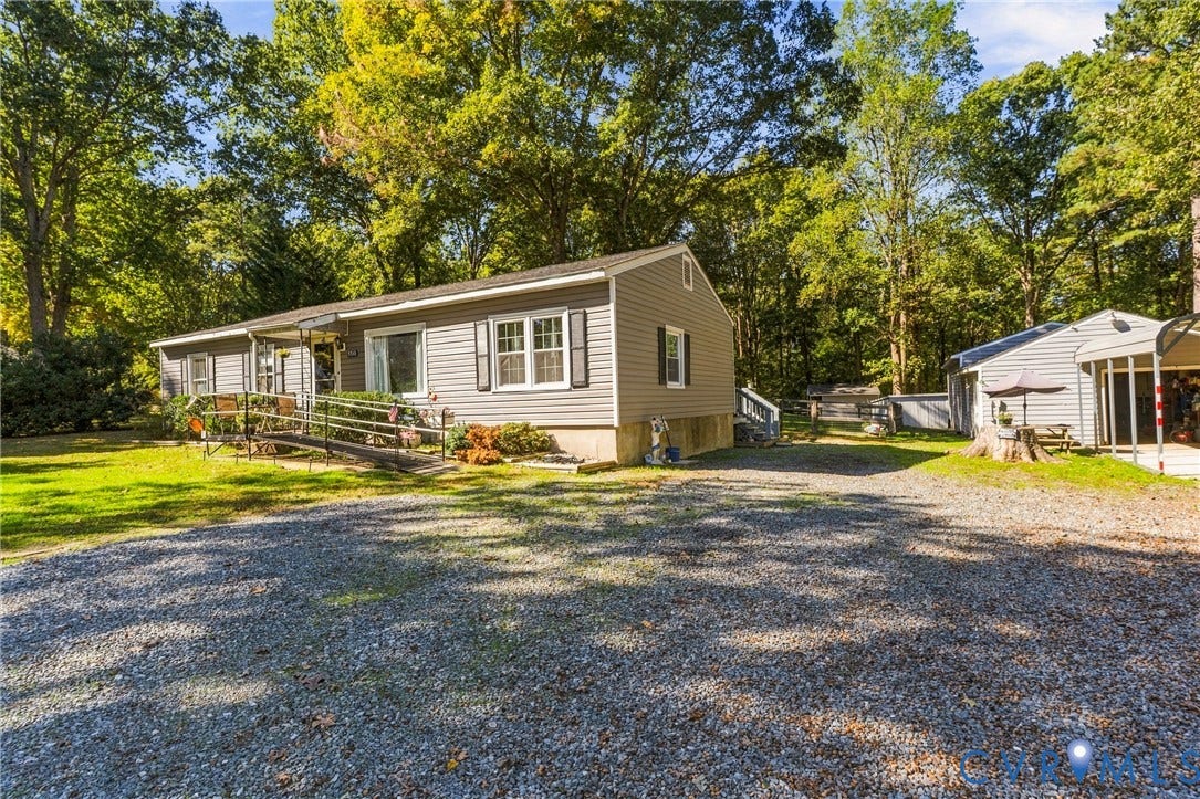 8840 Black Creek Road, New Kent, VA 23141 Single-story home featuring horizontal vinyl siding, a gravel driveway, a metal carport, and mature perimeter trees