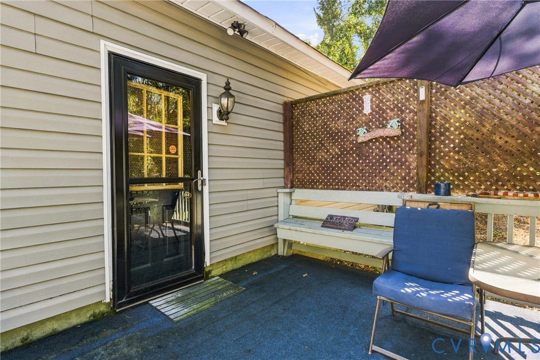 8840 Black Creek Road, New Kent, VA 23141 Exterior patio featuring light-toned horizontal siding, a full-lite glass door with paneled glazing, a built-in bench, and wood lattice privacy screening