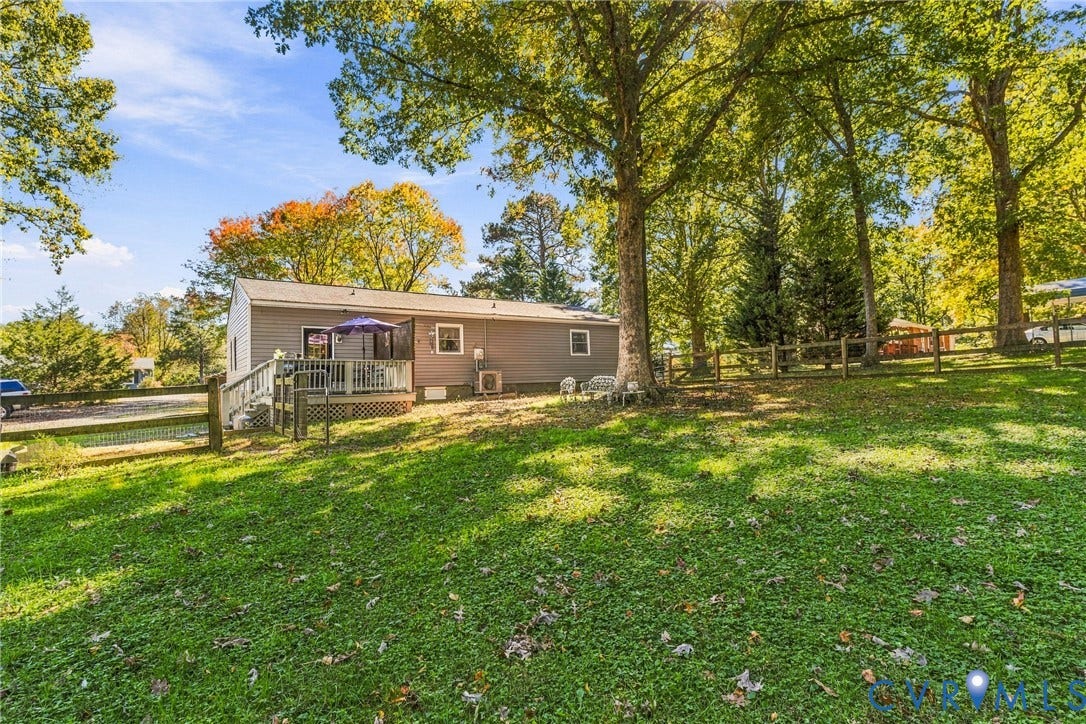 8840 Black Creek Road, New Kent, VA 23141 Exterior rear elevation featuring horizontal siding, a raised wooden deck with railings, and a fenced yard with mature trees