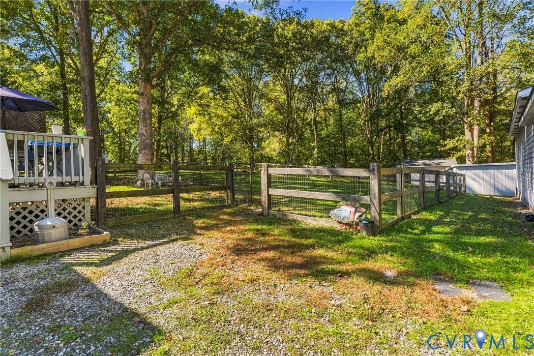 8840 Black Creek Road, New Kent, VA 23141 Rear exterior featuring a wood deck, gravel hardscaping, split-rail fencing with wire mesh, and mature perimeter trees