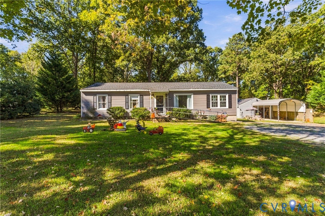 8840 Black Creek Road, New Kent, VA 23141 Single-story residence with horizontal siding, a gabled roof, multi-pane windows, and an attached metal-frame carport situated on a partially wooded lot