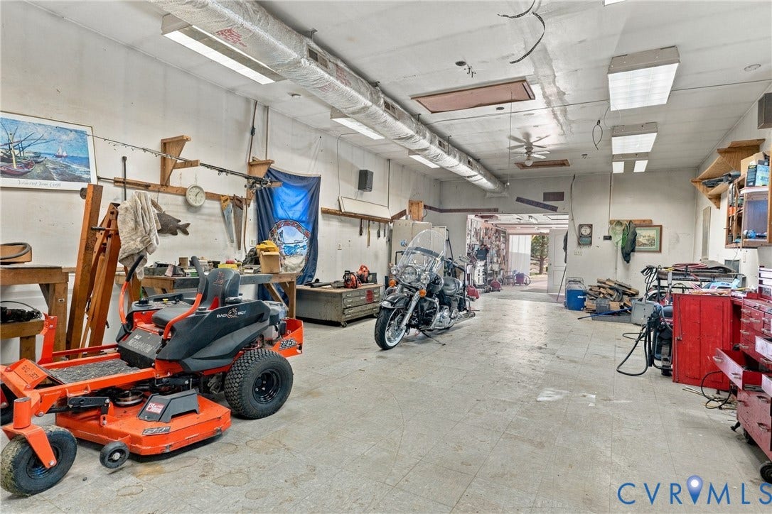 8840 Black Creek Road, New Kent, VA 23141 Expansive workshop space featuring concrete flooring, exposed overhead ductwork, multiple linear fluorescent light fixtures, and wall-mounted shelving units