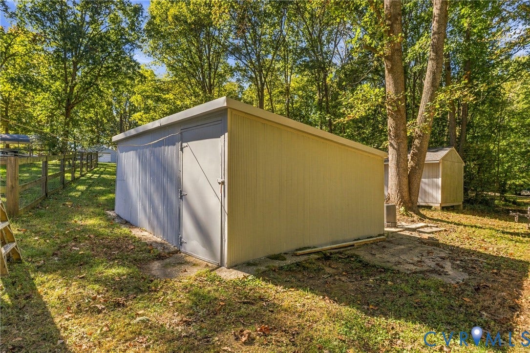 8840 Black Creek Road, New Kent, VA 23141 Detached storage structure with metal siding, a single-entry door, and a slanted roof, situated on a lot featuring mature trees and wood-post fencing