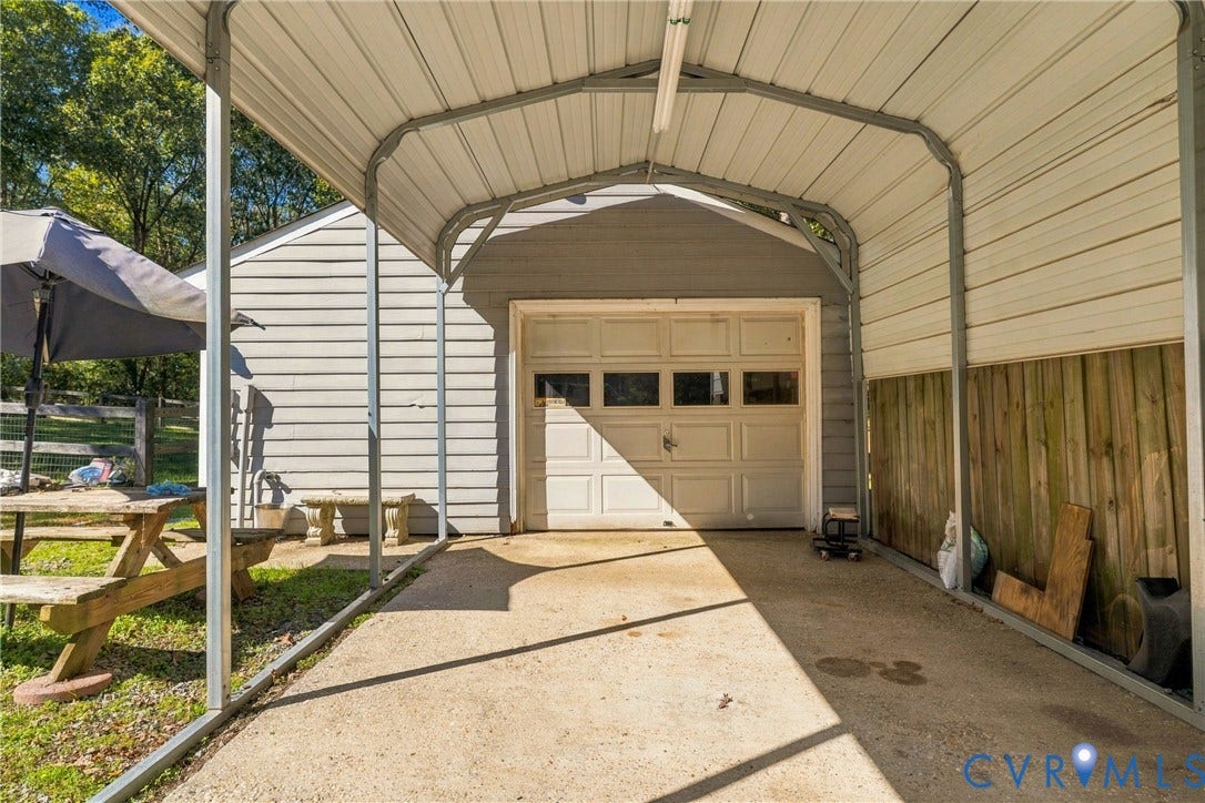 8840 Black Creek Road, New Kent, VA 23141 Metal-framed carport featuring a concrete parking pad, attached to a garage with a multi-panel sectional door and horizontal siding