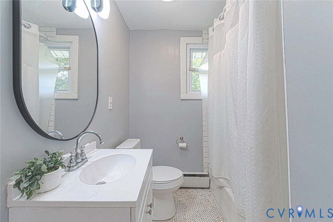 1818 Arlington Road, Hopewell, VA 23860 Bathroom featuring a white vanity with an integrated sink, polished chrome faucet, oval wall mirror, and tub-shower combination with white tile surround