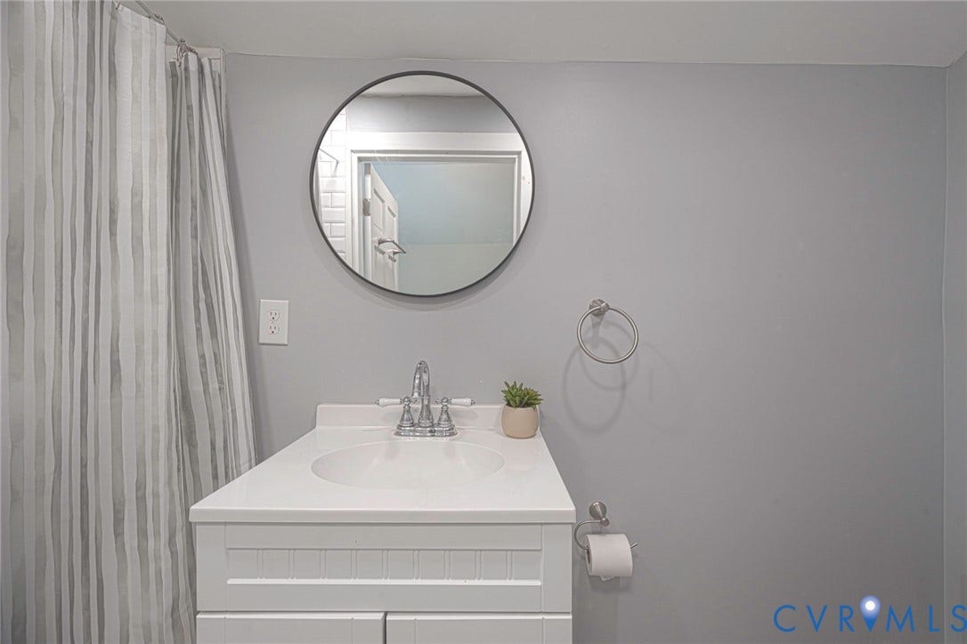 1818 Arlington Road, Hopewell, VA 23860 White vanity with an integrated countertop, circular mirror, metallic dual-handle faucet, and hardware accessories
