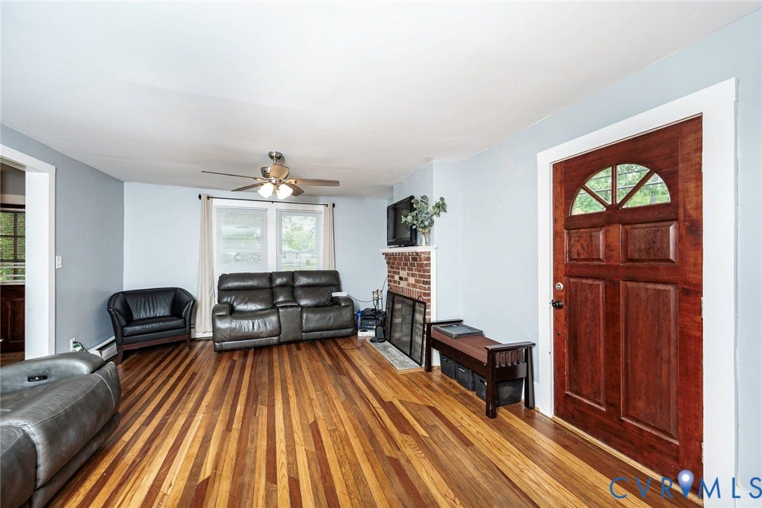 1818 Arlington Road, Hopewell, VA 23860 Wood-finish flooring, brick fireplace, and stained wood front door featuring an arched window detail and multipanel design, illuminated by a ceiling fan with integrated lighting